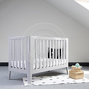 Interior of light baby room with a modern crib and woven wicker boxes for clothes or accessories