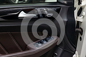 The interior of the luxury business car with a view of the drivers door with buttons, armrest and brown leather after detailing