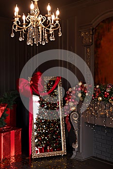 Interior of luxury dark living room with fireplace, comfortable sofa and chandelier decorated with Christmas tree and