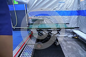 Interior of mobile plastic decontamination shower tent with small steel wash basin, mobile stretcher near