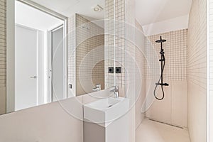 Interior of modern bathroom with beige tiles, shower and small sink