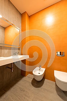 interior of modern bathroom in orange and white colors with toilet