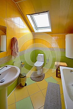 Interior of modern bathroom and toilet in attic room. Bath, toilet, trash can, hot water boiler mirror, dormer window