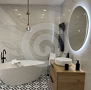 Interior of a modern bathroom. White tiles with black and white floor with bathtub and mirror