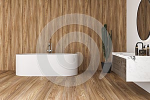 Interior of modern bathroom with white and wooden walls, floor and plants, comfortable white bathtub