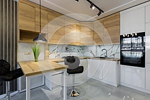 Interior of a modern kitchen, with a bar with wooden inserts and white marble tiles, in a small apartment
