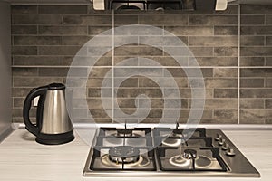 Interior of a modern kitchen. Close-up of electric kettle and gas hob on grey tile backsplash