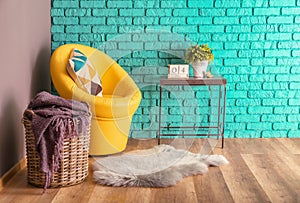 Interior of modern room with basket, armchair and houseplant on table near color wall