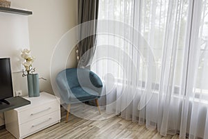 Interior of modern room with comfortable armchair near to large window with sheers and gray curtains