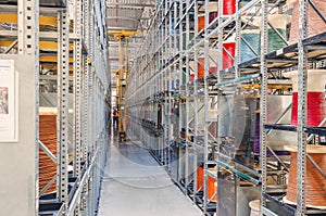 Interior of a modern storage warehouse with coils of colored cable on metal shelves. Forklift lift at the factory