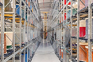 Interior of a modern storage warehouse with coils of colored cable on metal shelves. Forklift lift at the factory