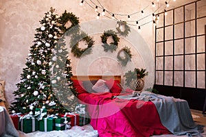 Interior of modern studio living room with comfortable bed decorated with Christmas tree and gifts