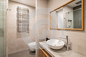 Interior of modern tiled bathroom with white toilet, radiator and shower in reflection of wooden framed mirror.