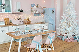 Interior of modern white kitchen with pink walls and blue decor on a Christmas New year eve. Pine tree with wrapped gifts and