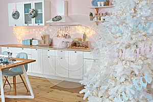 Interior of modern white kitchen with pink walls and decor on a Christmas New year eve. Pine tree with wrapped gifts and lights