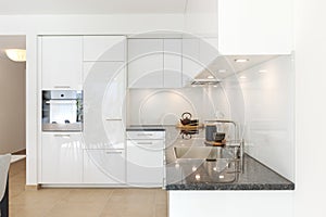 Interior of a new white corner kitchen. You can see the sink and also the oven. Elegant space with few things in sight. Marble