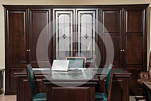 Interior of office room with laptop at wooden table and chairs