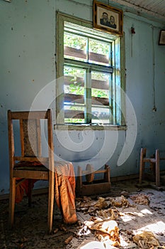 The interior of an old abandoned uninhabited house. An old wooden chair in a dirty, untidy room. Boarded up windows with wooden