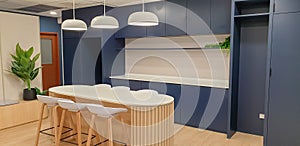 Interior photography of a modern office breakout area with kitchen, blue and grey cabinets, orange pendant lights, polished