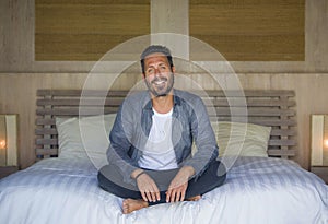 Interior portrait of 30s happy and handsome man at home in casual shirt and jeans sitting on bed relaxed at home smiling confident
