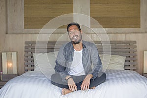 Interior portrait of 30s to 40s happy and handsome man at home in casual shirt and jeans sitting on bed relaxed at home smiling