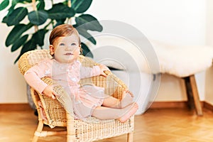 Interior portrait of adorable baby girl sitting on wicker chair