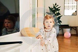 Portrait of funny toddler girl trying to open drawer