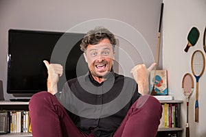 Interior portrait of handsome joyful happy man with thumbs up in home living room happiness in house