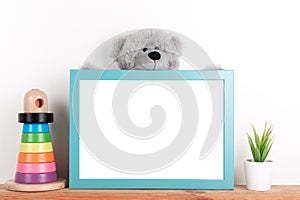 Interior poster mock up for nurcery, children`s room with vertical wooden frame, toys and teddy bear on white wall background