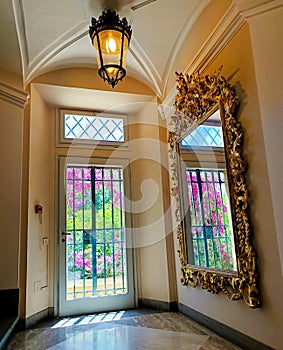 Interior of the Roman building with nice barroco style mirror which reflects the garden exit door and pink blossom flowers photo