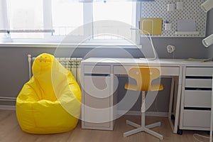 The interior of the room of a boy or girl student in light white and yellow tones, the student's desk in the room at