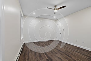 Interior of a room with a parquet floor,baseboard heater on the white wall, a ceiling fan and a door