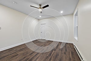 Interior of a room with a parquet floor, white walls,baseboard heater under the window,a ceiling fan