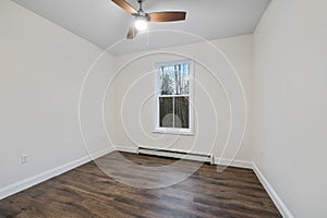 Interior of a room with a parquet floor,white walls,ceiling fan and baseboard heater under window