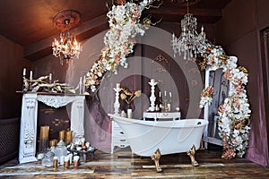 The interior of the room is in vintage style. Large bathtub and fireplace. Decoration with flowers