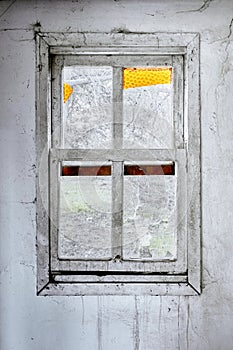 Interior of a ruined house with old, dirty and cracked white wall and a broken window frame with a green meadow field view