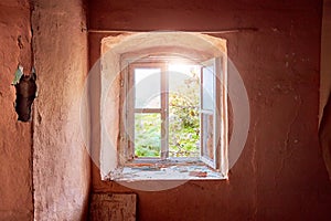Interior of a ruined old cottage with a light pink wall and a broken wooden window frame viewing a rural green meadow field