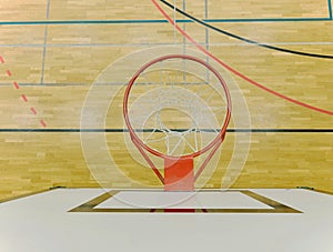 Interior of school gym with basketball board and basket. Safety nets over windows.