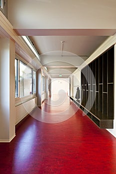 Interior of a school with long corridors with red floors.