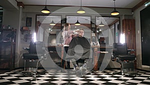 Interior shot of working process in modern barbershop. Side view portrait of attractive young man getting trendy haircut