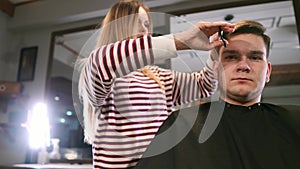 Interior shot of working process in modern barbershop. Side view portrait of attractive young man getting trendy haircut