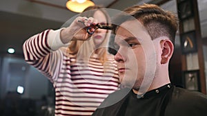 Interior shot of working process in modern barbershop. Side view portrait of attractive young man getting trendy haircut
