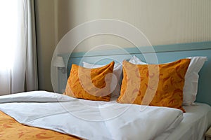 The interior of a small inexpensive hotel room for two persons with double bed. The bed is covered with orange blanket and orange