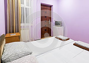 Interior of a small room with a double bed, a window, a TV and a fridge