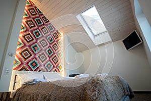 Interior of a spacious hotel bedroom on attic floor with fresh linen on a big double bed. Cozy contemporary mansard room in a