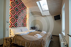 Interior of a spacious hotel bedroom on attic floor with fresh linen on a big double bed. Cozy contemporary mansard room in a