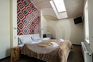 Interior of a spacious hotel bedroom on attic floor with fresh linen on a big double bed. Cozy contemporary mansard room in a