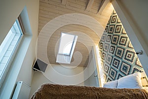 Interior of a spacious hotel bedroom on attic floor with fresh linen on a big double bed. Cozy contemporary mansard room in a