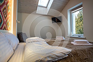 Interior of a spacious hotel bedroom on attic floor with fresh linen on a big double bed. Cozy contemporary mansard room in a