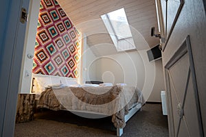 Interior of a spacious hotel bedroom on attic floor with fresh linen on a big double bed. Cozy contemporary mansard room in a
